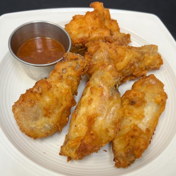 Golden fried chicken wings with a side of dipping sauce on a white plate.