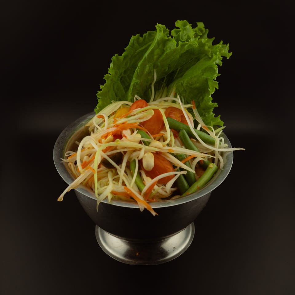 Som Tum, a Thai papaya salad with green beans, tomatoes, and peanuts in a metal bowl.