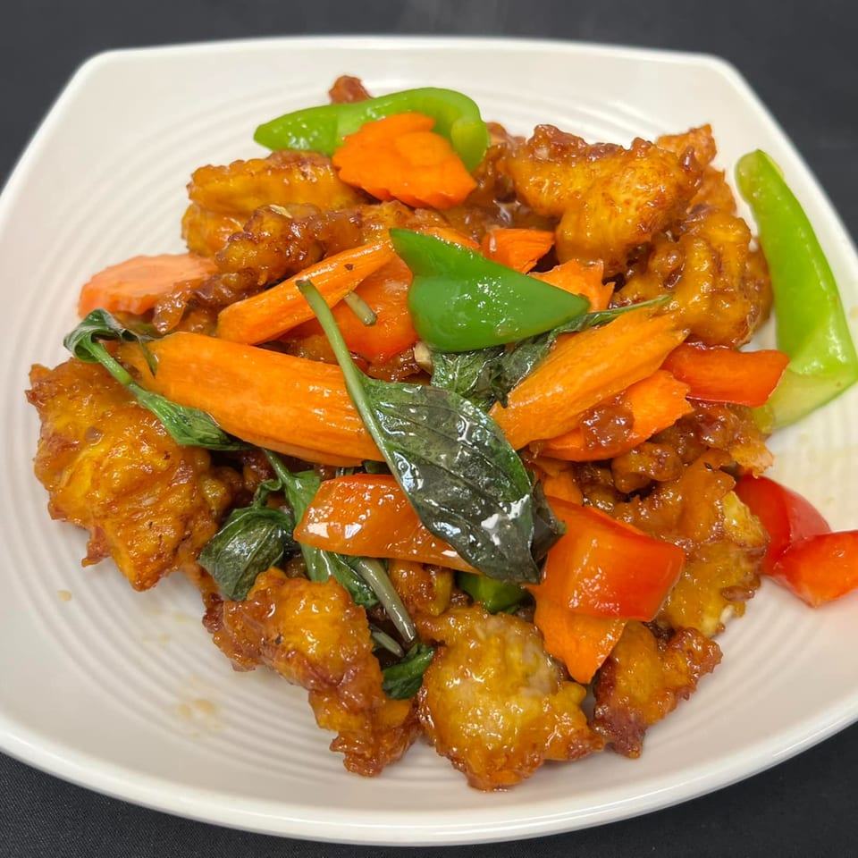 Tuk Tuk Thai Campbell's crispy chicken stir-fry with carrots, bell peppers, and basil on a white plate.