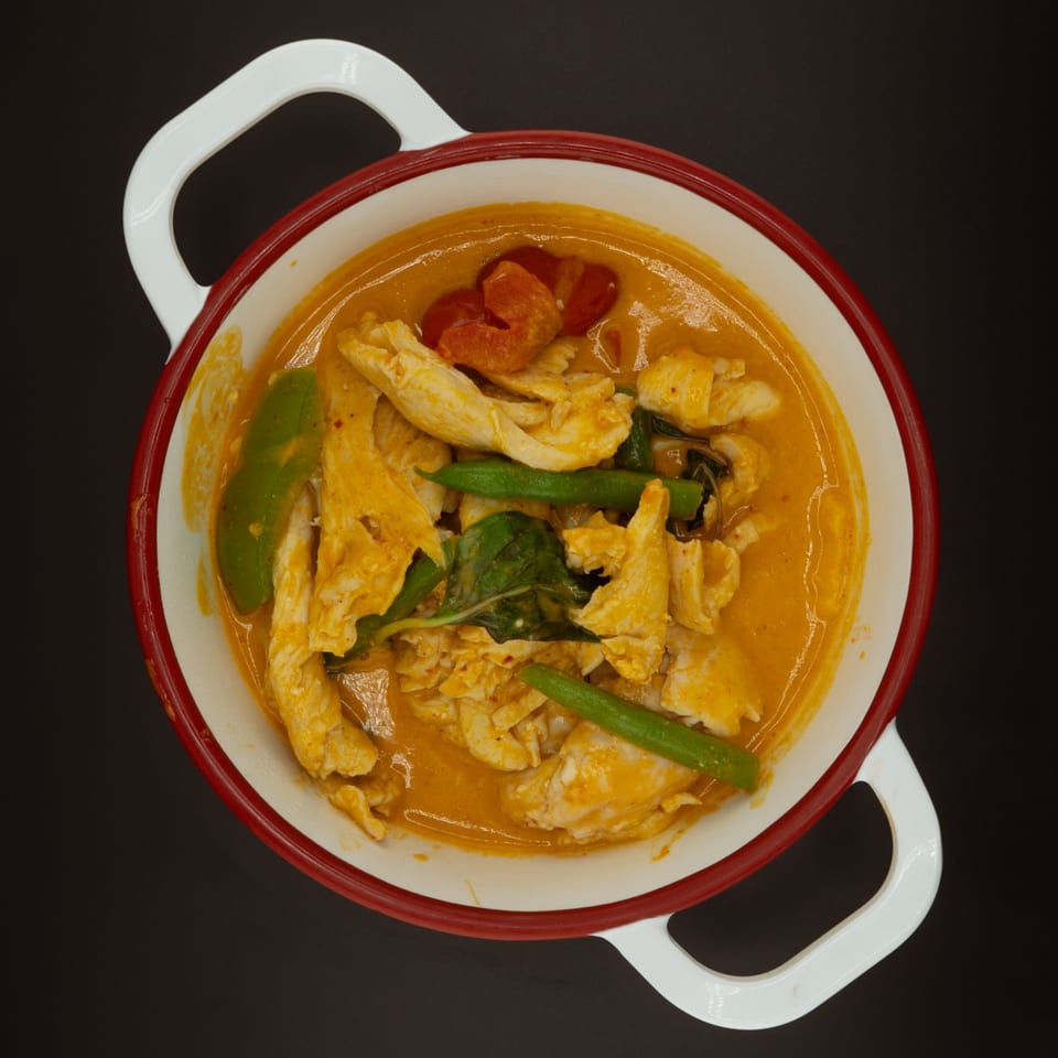 Tuk Tuk Thai red curry with chicken, green beans, and bell peppers in a white and red bowl.