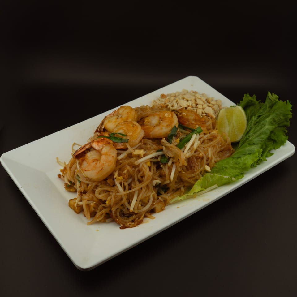 Shrimp Pad Thai with noodles, bean sprouts, peanuts, lime, and lettuce on a white plate.