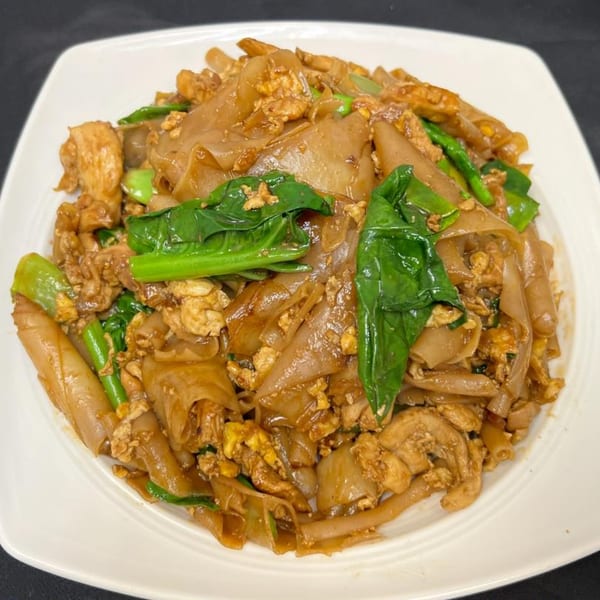 A close-up of Pad See Ew with wide rice noodles, chicken, egg, and green Chinese broccoli.