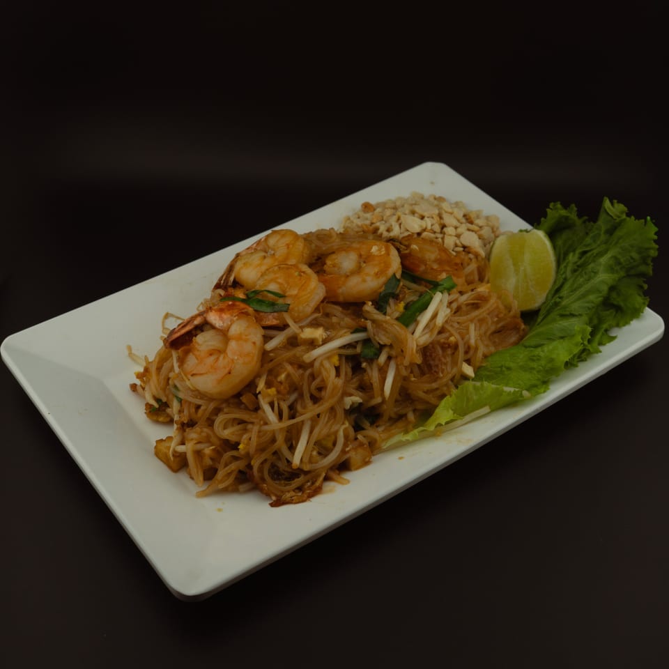 Shrimp Pad Thai with bean sprouts, peanuts, lime, and lettuce on a white rectangular plate.
