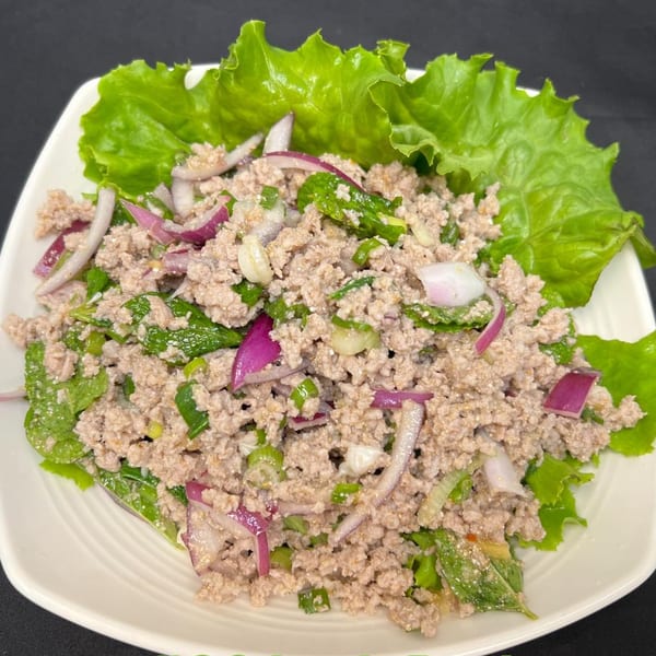 Close-up of a Thai Larb dish with minced meat, red onions, and green herbs on lettuce.