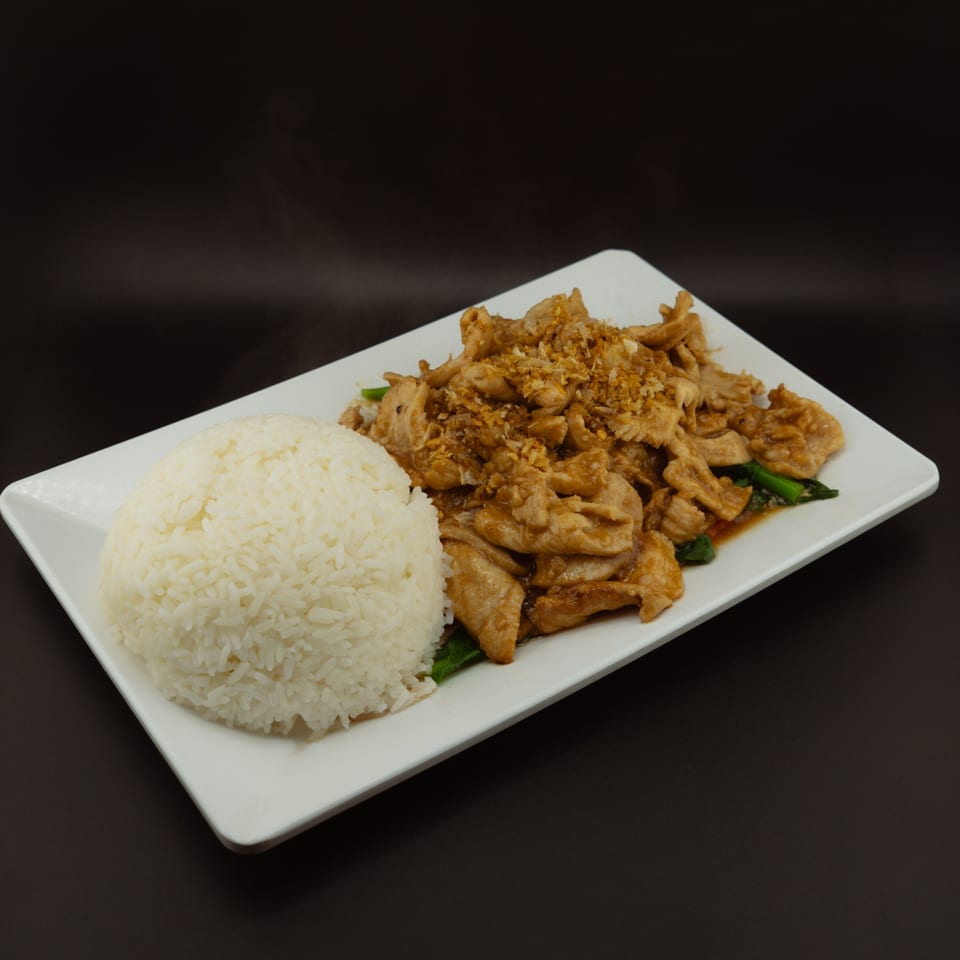 Garlic chicken with fried garlic and green vegetables, served with a side of white rice.