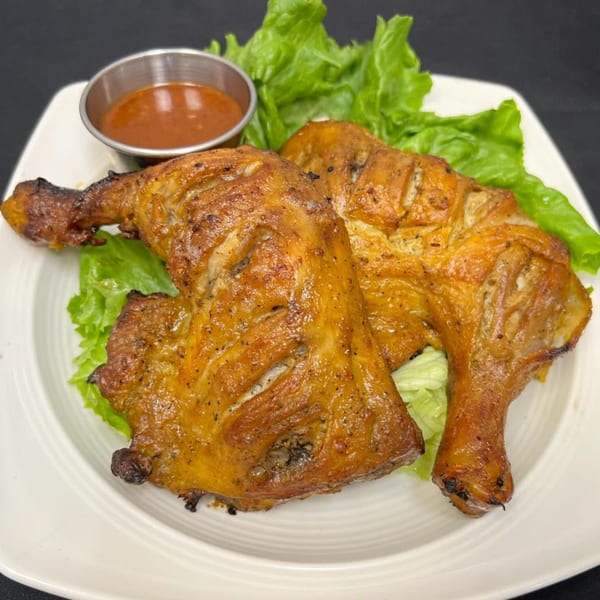 Two golden-brown grilled chicken leg quarters with a side of dipping sauce and lettuce on a white plate.
